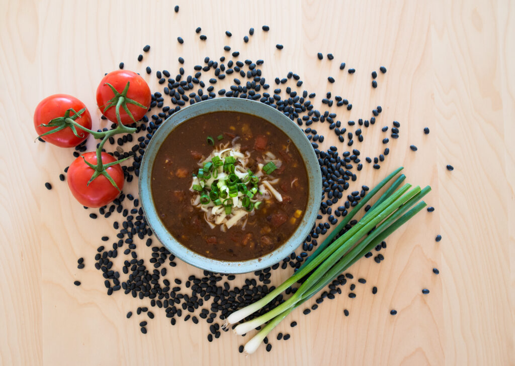 Black Bean Soup from Greentree Cooperative in Mount Pleasant, MI. Bowl is surrounded in black beans, tomatoes and green onion.