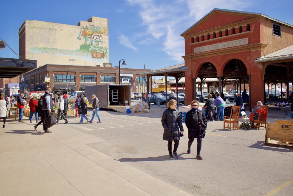Winter at the Eastern Market as many patrons walk between sheds, with a mural in the background. 