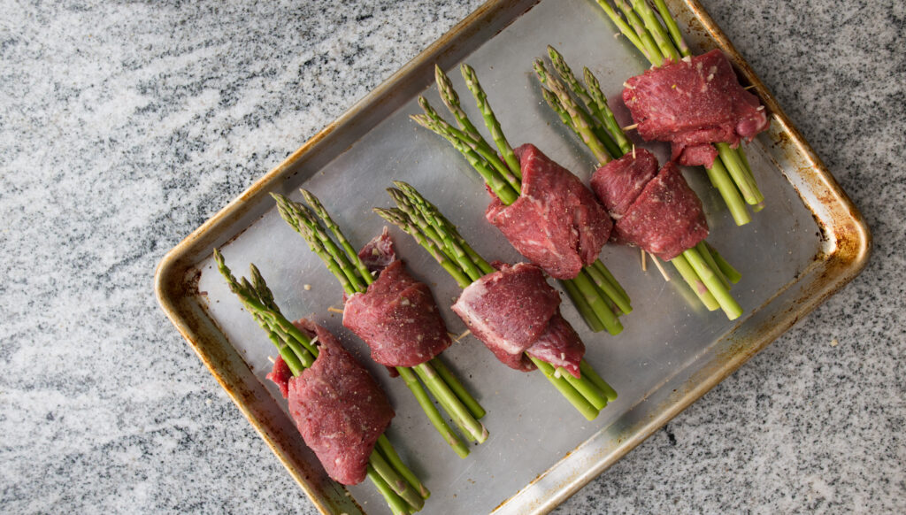 Asparagus and ribeye rollatini before the grill on a sheet pan. 