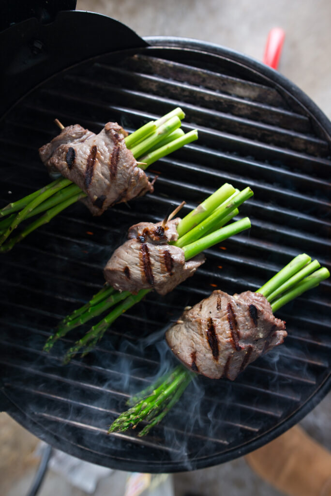 Asparagus and ribeye rollatini on the grill with smoke and grill marks. 