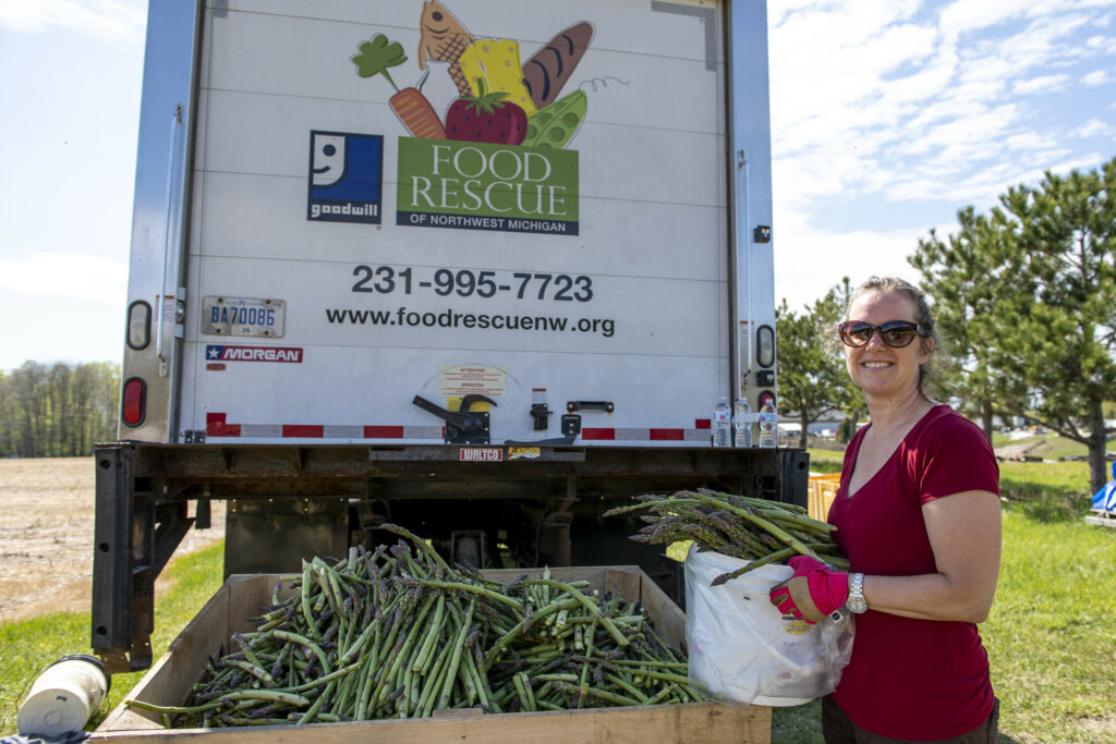 A volunteer smiles with gleaned asparagus behind a Food Rescue van