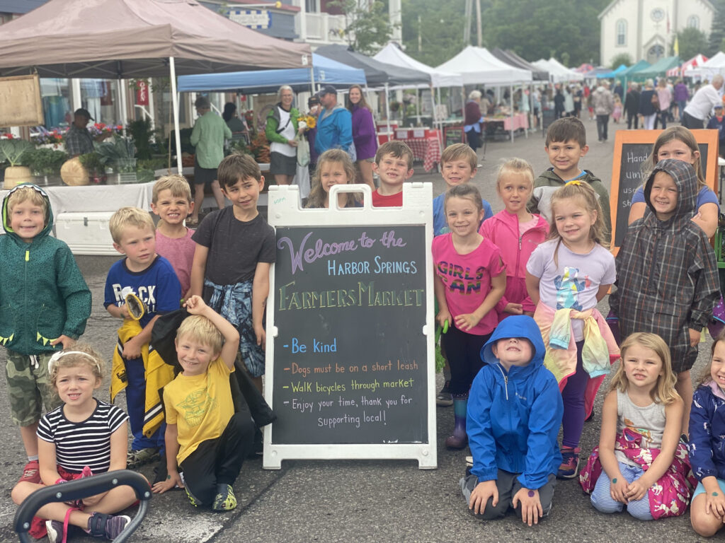 Children gather around a sign for the Harbor Springs Farmers Market