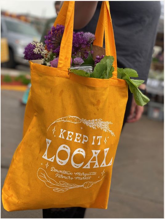A market tote with the phrase Keep It Local is filled with flowers and radish greens at the Marquette Farmers Market
