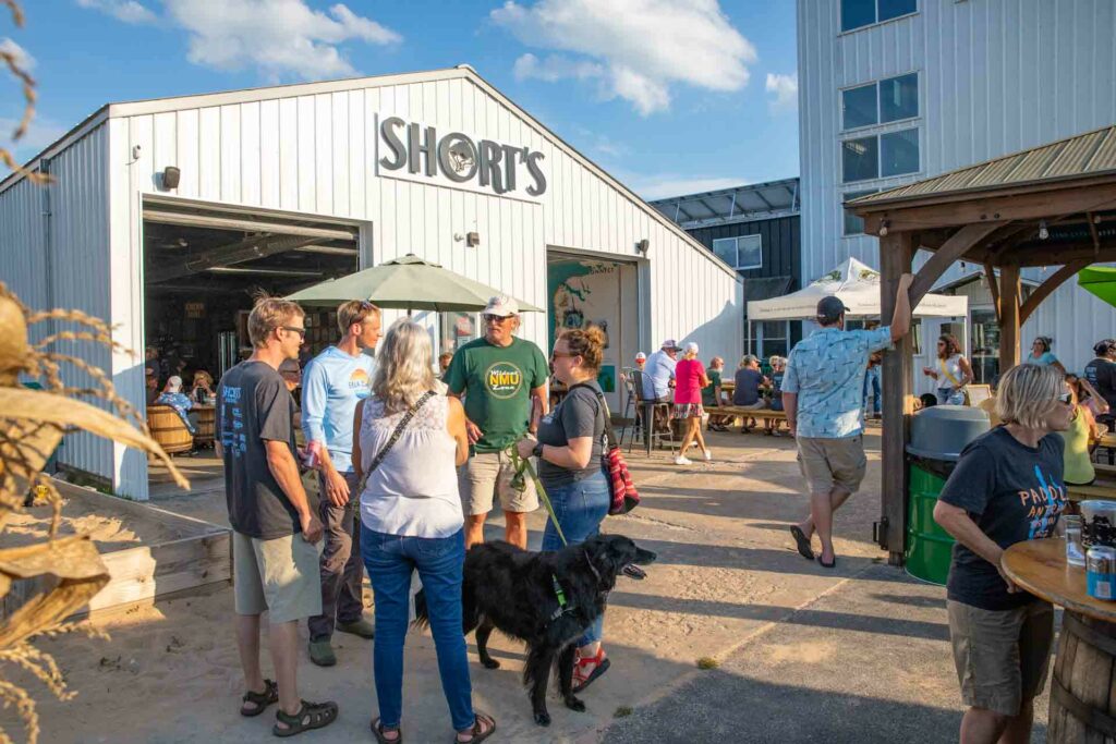 Short's Pull Barn in Elk Rapids with a crowd in front wearing tee shirts and shorts, with a dog. Photo credit: Short's Brewing 