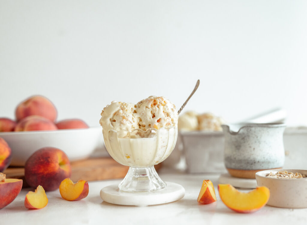 Peach Crumble Ice Cream in a small bowl with fresh peaches. Photo Credit: Taste the Local Difference