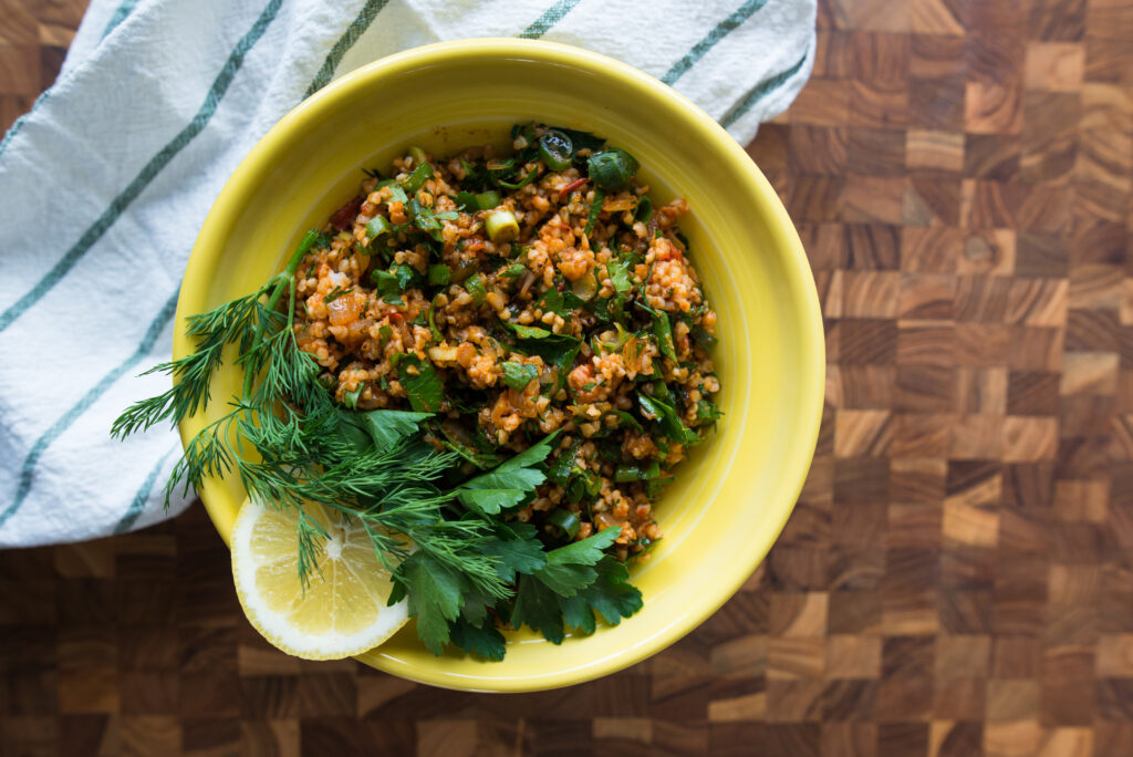 A Turkish bulgur salad, kisir, is presented in a yellow bowl with fresh herbs. 